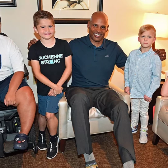 A man sitting in a chair with two young boys standing beside him, one wearing a 