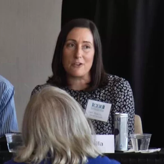 Woman speaking at a panel discussion, wearing a name tag with the ICER logo.