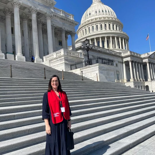 Woman standing on the steps of the U.S. Capitol building, wearing a red scarf and smiling.