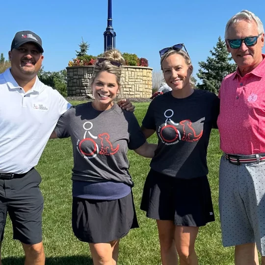 Four people smiling and posing together outdoors at an event, two of them wearing matching foundation t-shirts.