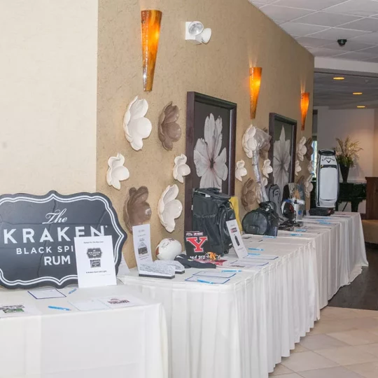 Display table at an event featuring various items for auction, including a Kraken Black Spiced Rum sign and sports memorabilia.